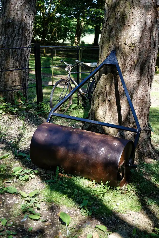 Old metal lawn roller resting beneath trees in an Essex garden